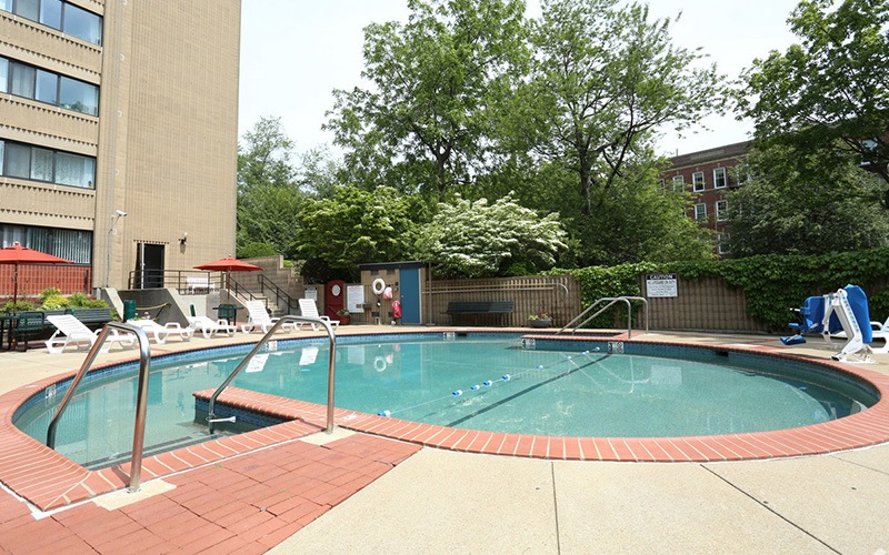 spacious swimming pool with reclining seats, near green landscaping and with nearness to property buildings